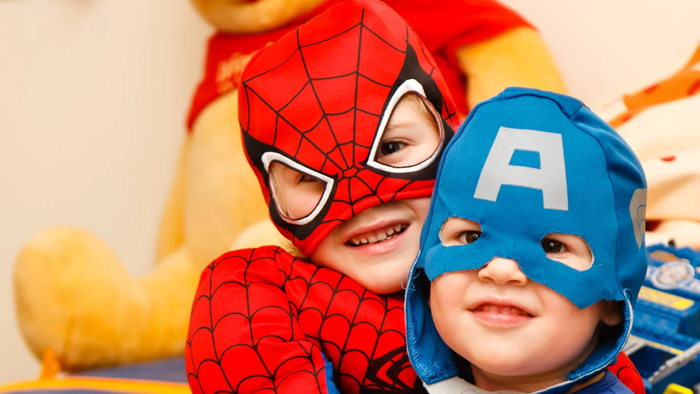 To børn i superheltekostumer, det ene som Spider-Man og det andet som Captain America, smiler til kameraet.