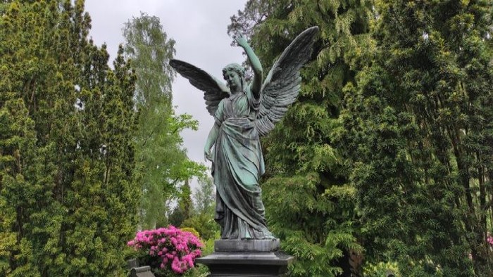 Engelsstatue in grünem Park mit rosa Blumen