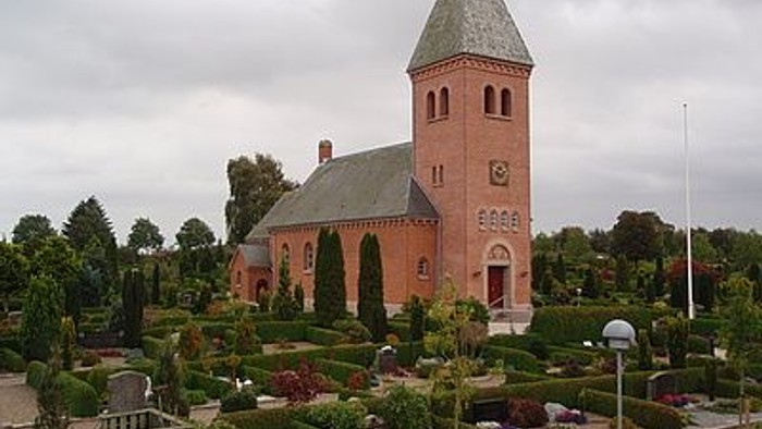 En rød kirke med højt tårn og en have med blomster.