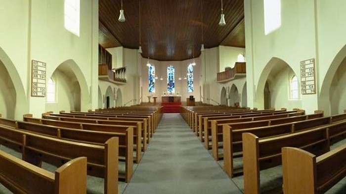 Leere Kirchenbankreihen vor Altar in heller Kirche
