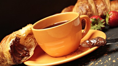Ein orange Tasse mit Kaffee und ein Croissant mit Schokolade auf einem Teller