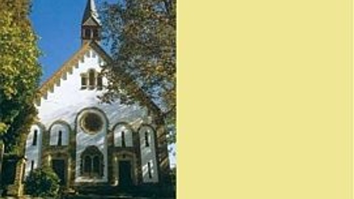 Kleine Kirche mit spitzem Turm und Bogenfenstern, umgeben von Bäumen