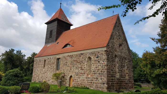 Kleine Steinkirche mit rotem Dach und Turm in ländlicher Umgebung