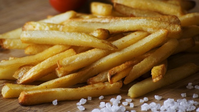 Gulde fritureret kartoffelstenger med salt og tomat i baggrunden