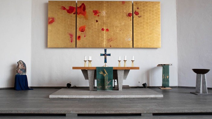 Ein Kircheninneres mit Altar, Kerzen und einem großen goldenen Bild mit roten Blumen an der Wand