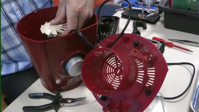 Person repariert ein rotes Elektrogerät mit Werkzeugen auf einem Tisch