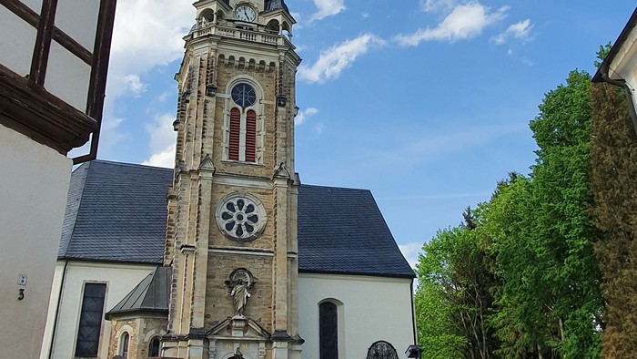 Kirchturm mit Uhr und Kreuzigungsgruppe vor weißem Gebäude