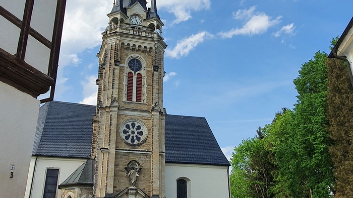 Kirchturm mit Uhr und Kreuzigungsgruppe vor weißem Gebäude