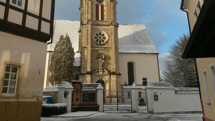 Gotischer Kirchturm mit Uhr und Kreuzigungsgruppe vor historischem Hintergrund