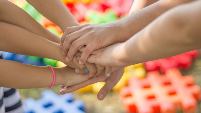 Viele Hände bilden ein Gebinde, farbenfrohe Puzzleteile im Hintergrund