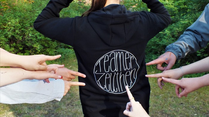 Mehrere Hände zeigen auf das T-Shirt einer Person mit der Aufschrift