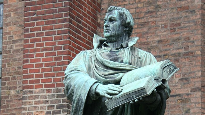  Statue eines Mannes mit Buch vor Ziegelmauer