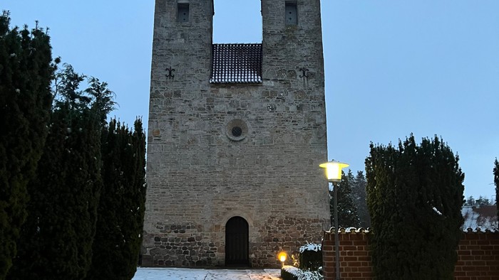 En snedækket sti leder op til en middelalderlig stenkirke med to tårne.