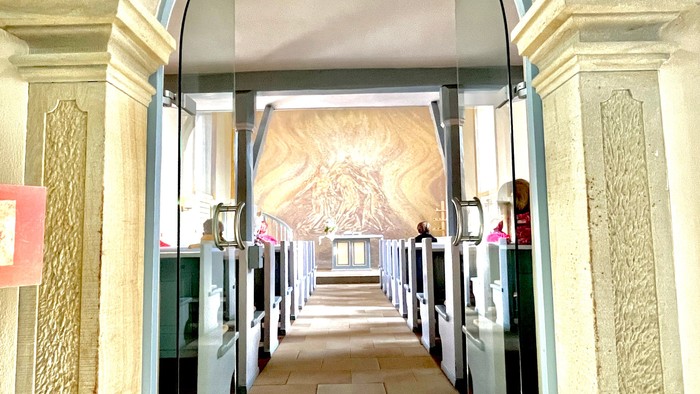 Kircheninneres mit bogigem Durchgang und Buntglasfenster.