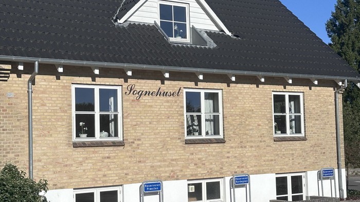 To-etagers murstensbygning med sort tag og hvide kanter, mærket