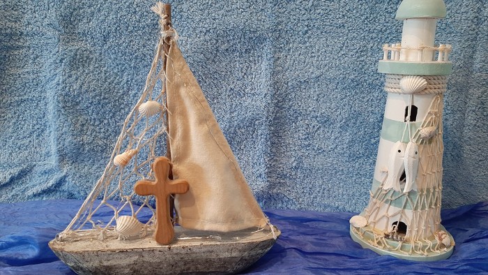 Ein hölzernes Segelboot und ein Leuchtturm-Dekorationsstück vor blauem Hintergrund