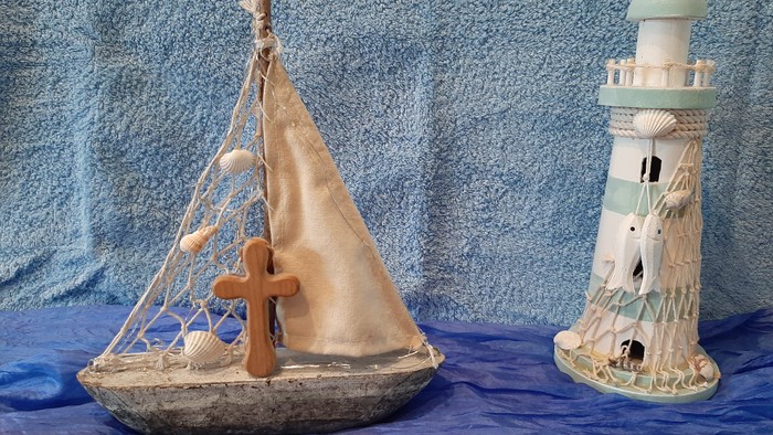 Ein hölzernes Segelboot und ein Leuchtturm-Dekorationsstück vor blauem Hintergrund