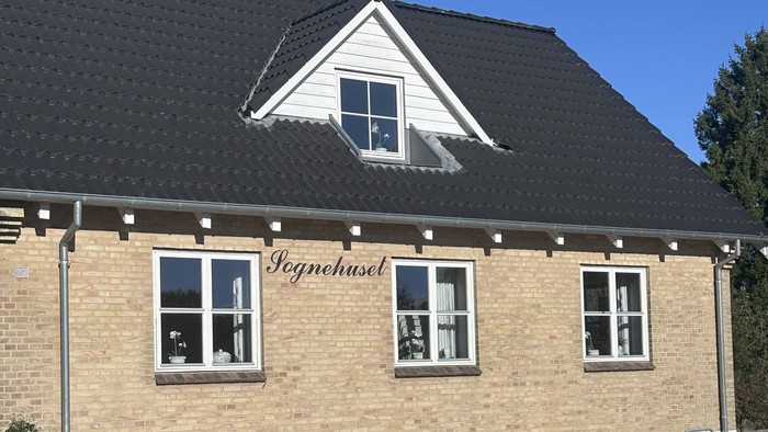 To-etagers murstensbygning med sort tag og hvide kanter, mærket