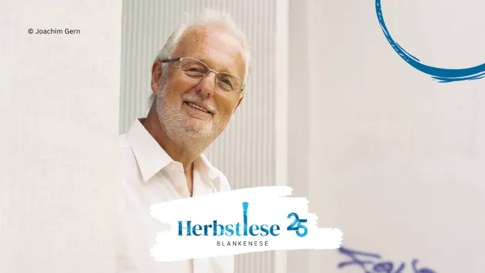 Ein älterer Mann mit Brille lächelt vor einem weißen Hintergrund mit dem Herbstlese-Logo.
