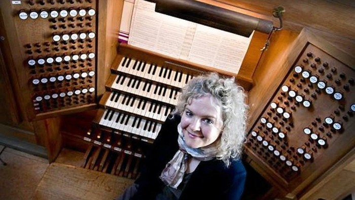 Kvinde sitter ved et orgel og smiler.