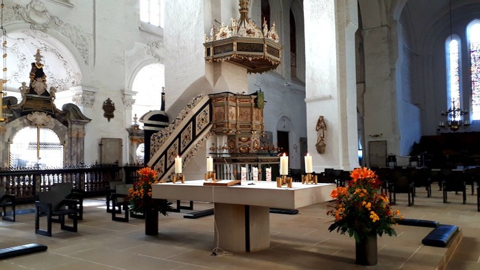 Innenraum einer Kirche mit Altar, Kanzel und Blumenarrangements