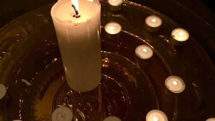 Et tændt stearinlys omgivet af mindre stearinlys i en dekorativ beholder.