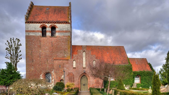 En rød murstenskirke med spiret og gravhøje i forgrunden