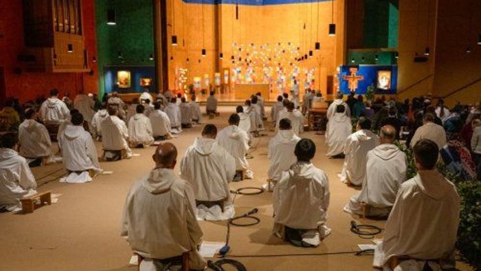 Eine Gruppe von Menschen in weißen Roben sitzt in einem Raum und meditiert.