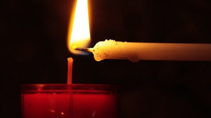 Ein brennender Docht wird über einer roten Kerze gehalten