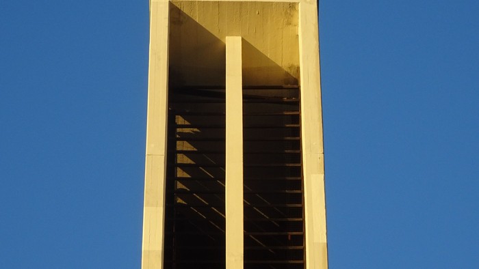 Ein weißer Glockenturm mit Kreuz vor blauem Himmel