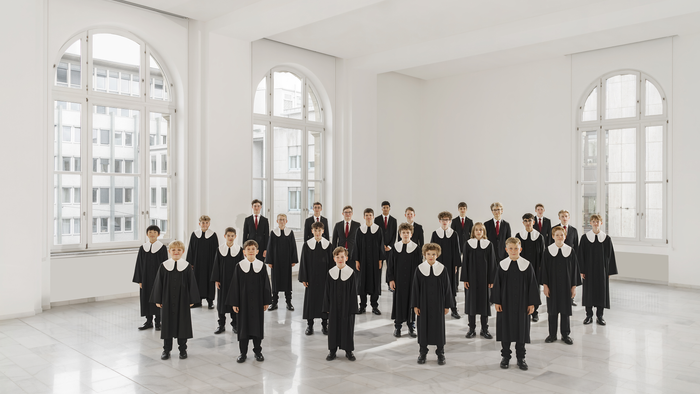 Gekleidete Chormitglieder posieren formell in einem geräumigen, hellen Raum mit großen Bogenfenstern.