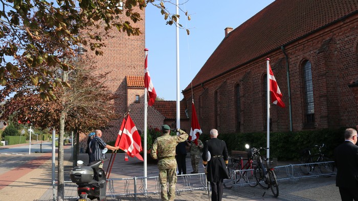 En gruppe personer hylder flag i forvejen af et rødt mursteinsbygning.