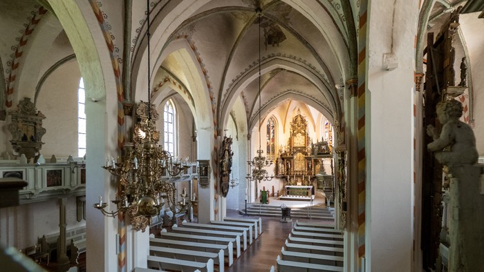 Innenraum einer Kirche mit hohen Bögen, Kirchenbänken und einem Altar am Ende.