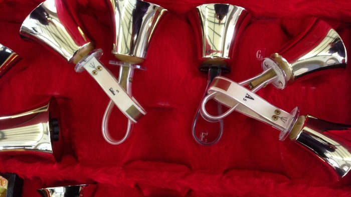 Several silver handbells with handles, some with red ribbons, arranged on red velvet.