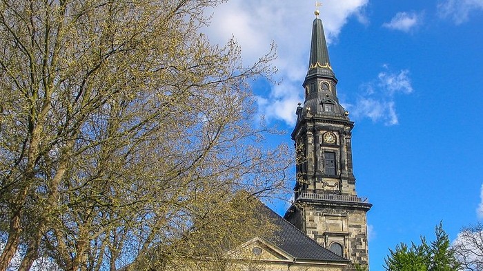 En kirke med høj tårn og klokkeface under et blødt blå himmel.