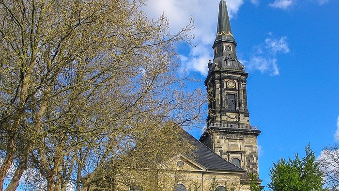 En kirke med høj tårn og klokkeface under et blødt blå himmel.