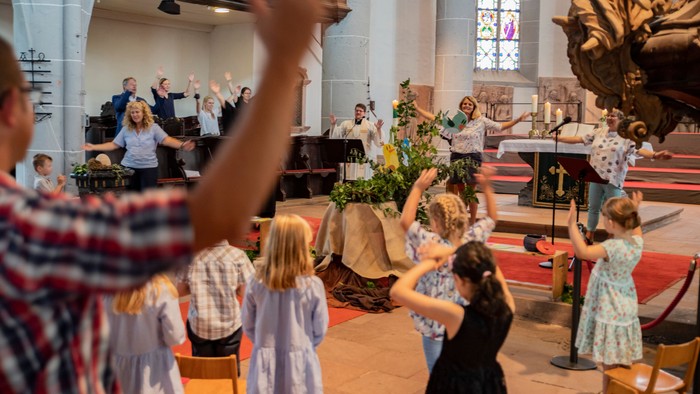 Kinder und Erwachsene heben die Arme in einer Kirche während eines Gottesdienstes.