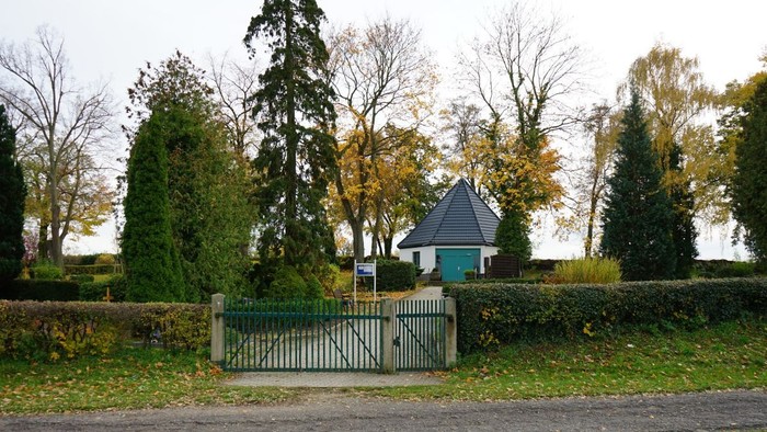 Blick auf ein kleines, weißes Gebäude mit blauem Dach hinter einem grünen Metalltor.