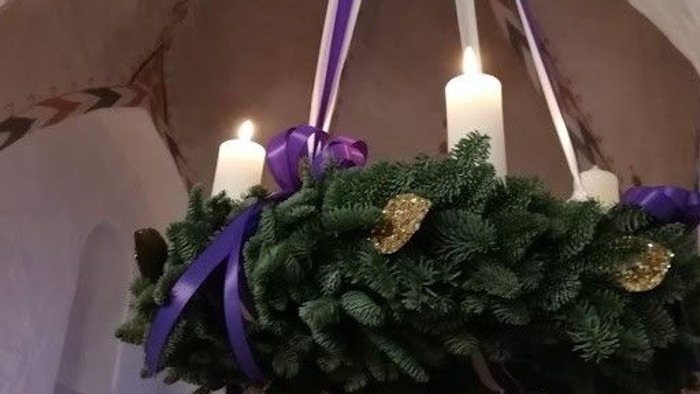 En hængende kranse med grønne blade, lys og violette bænder i et rum med bueformet loft