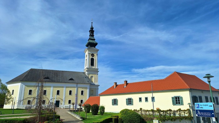 Weiße Kirche mit hohem Turm und rotem Dach auf grünem Grund.