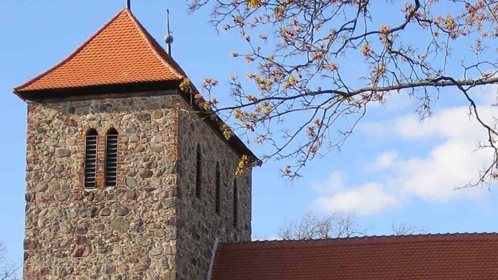 Steinige Kirche mit hohem Turm und rotem Dach unter blauem Himmel