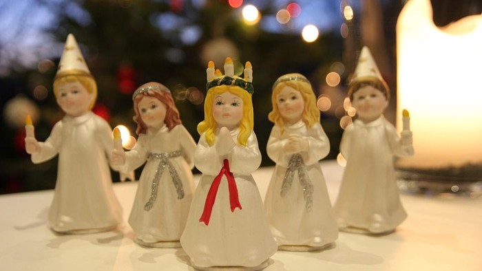 Fire lille julepiger med hårbånd og hvidt tøj står i en række foran en juletree.