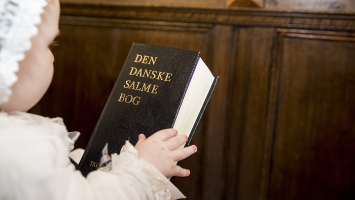 Børn med hvid kappe holder en bog med den danske salmebog
