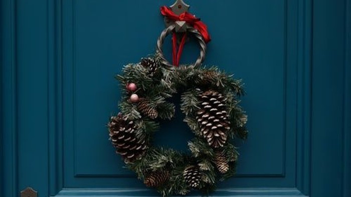 En julekrans med nåler og en rød stjerne hænger på en blå dør.