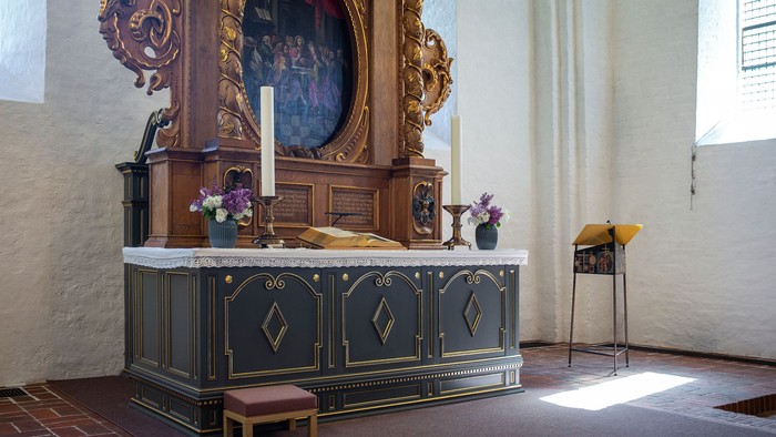 En altertavle med blomster og lysstake i kirke.