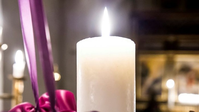En tændt hvid lysestage omgivet af lilla blomster i en blødt sløret, varmt oplyst omgivelse.