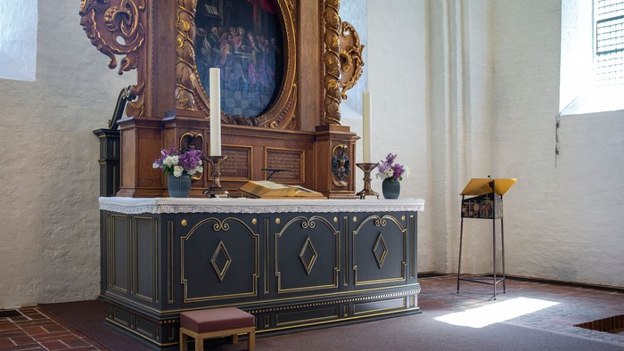 En altertavle med blomster og lysstake i kirke.