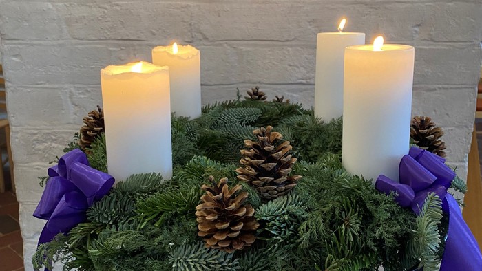 En adventskranse med fire lysende lygter og nødder på en hvid kamin.