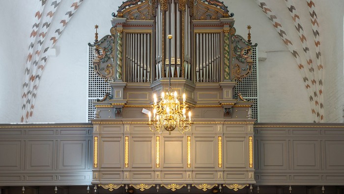 Elegant kirkeinteriør med træbænke, et stort orgel og prægtig loftsbelysning.