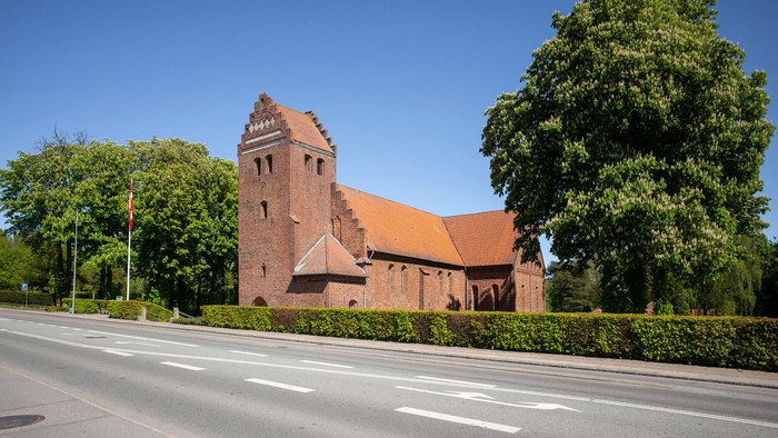 En rød murstenskirke med tårn ved en vej